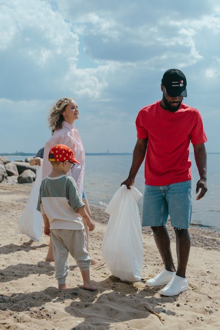 A person wearing a light blue t-shirt, black shorts, and white sneakers with green accents is standing on a rocky shoreline, using a trash picker tool to pick up litter from the uneven, moss-covered r